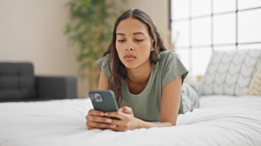 African american woman using smartphone lying on bed at bedroom