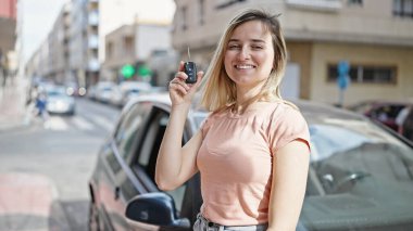Genç sarışın kadın gülümsüyor. Elinde yeni arabanın anahtarı var.