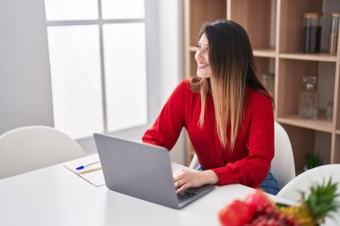 Evdeki masada oturan genç İspanyol kadın dizüstü bilgisayar kullanıyor.