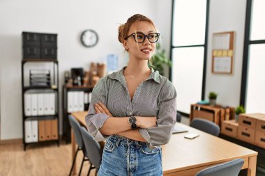 Beyaz kadın iş kadını gülümseyen, kendine güvenen, kollarını kavuşturup ofiste el kol kola duran.