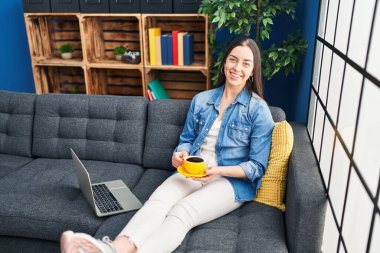 Genç ve güzel İspanyol kadın dizüstü bilgisayar kullanıyor. Evde kahve içiyor.