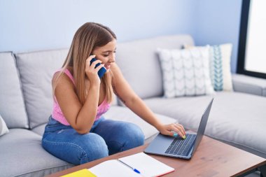 Young beautiful hispanic woman student sitting on sofa talking on smartphone at home