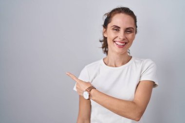 Güzel esmer kadın izole edilmiş arka planda neşeli bir şekilde ayakta duruyor yüzünde gülümseme, mutlu ve doğal bir ifadeyle elleri ve parmaklarıyla yüzünü işaret ediyor. 