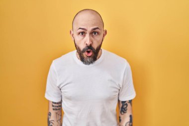 Sarı arka planda dikilen İspanyol dövmeli genç adam şaşkınlık ve şaşkınlık ifadesi, korku ve heyecan dolu yüz ifadesiyle dehşete düşmüş ve şok olmuştu.. 