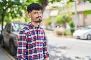 Young hispanic man smiling confident looking to the side at street