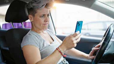 Young woman using smartphone sitting on car at street