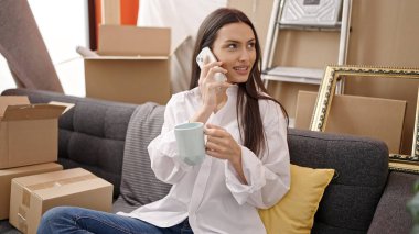 Genç, güzel, İspanyol bir kadın kahve içiyor. Yeni evinde akıllı telefondan konuşuyor.