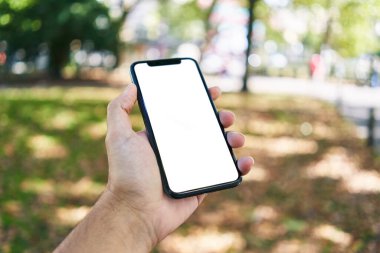 Akıllı telefonu tutan adam parkta beyaz ekranı gösteriyor.