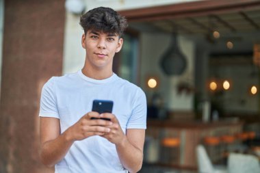 Young hispanic teenager smiling confident using smartphone at street
