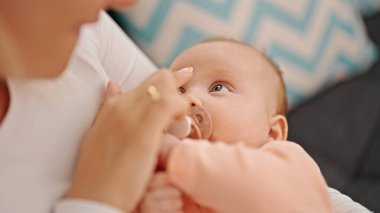 Anne ve kızı kanepede oturmuş emziriyorlar.