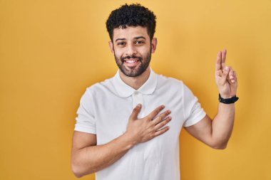 Sarı arka planda duran Arap adam gülümsüyor, elleri göğsünde ve parmakları havada yemin ediyor, sadakat yemini ediyor. 