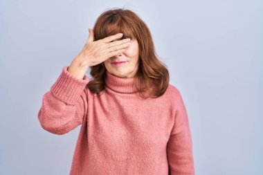 Middle age hispanic woman standing over isolated background covering eyes with hand, looking serious and sad. sightless, hiding and rejection concept 