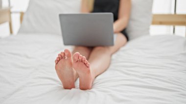 Yatak odasında dizüstü bilgisayar kullanan genç sarışın kadın.