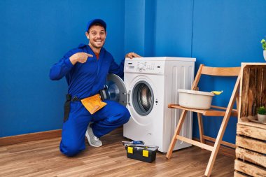 Çamaşır makinesinde çalışan genç İspanyol adam gülümseyen mutlu ve gururlu birini işaret ediyor. 