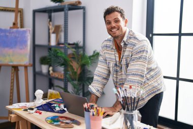Genç İspanyol ressam resim stüdyosunda dizüstü bilgisayar kullanıyor.