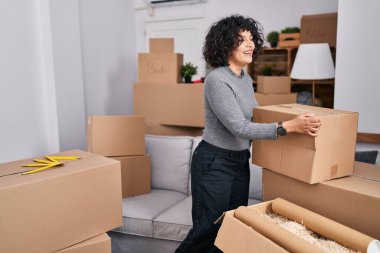Young beautiful hispanic woman smiling confident holding package at new home
