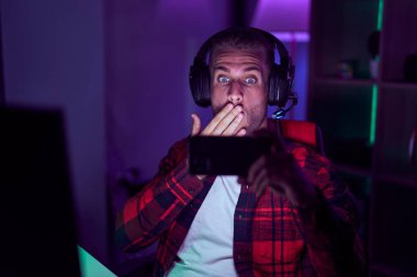 Akıllı telefonlu video oyunları oynayan genç beyaz bir adam ağzını eliyle kapatıyor, şok geçiriyor ve hata yapmaktan korkuyor. şaşırmış ifade 