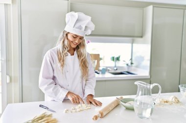 Young woman wearing cook uniform counting small pasta dough at kitchen