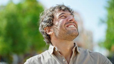 Young hispanic man smiling confident looking to the sky at park