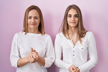 Orta yaşlı anne ve küçük kızı pembe arka planda el ele tutuşup rahatça gülümsüyor. Başarı ve iyimserlik 