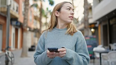 Sokakta akıllı telefon kullanan genç sarışın kadın.