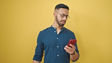 Akıllı telefon kullanan İspanyol genç adam izole edilmiş sarı arka plan yüzünden üzgün.