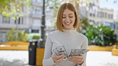 Parkta kendine güvenen genç sarışın kadın gülümsüyor.