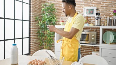 Afro-Amerikalı aşçı yemek odasında akıllı telefondan internet tarifi arıyor.