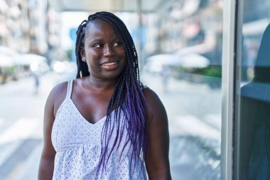 Afro-Amerikalı kadın gülümsüyor. Kendinden emin bir şekilde caddeye bakıyor.