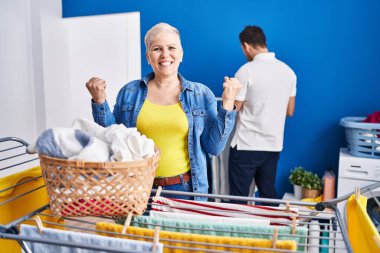 İspanyol anne ve oğlu çamaşır ipine kıyafet asıyor. Gururla bağırıyor, zaferi kutluyor ve kollarını kaldırarak başarıyı kutluyorlar. 
