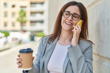 Genç iş kadını akıllı telefondan konuşuyor. Sokakta kahve içiyor.
