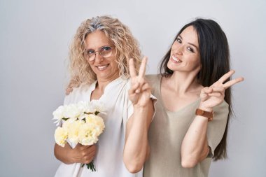 Anne ve kızı ellerinde bir buket beyaz çiçekle kameraya bakıp zafer işareti yapıyorlar. İki numara.. 