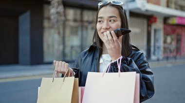 Güzel İspanyol bir kadın elinde alışveriş torbalarıyla akıllı telefonuyla sesli mesaj yolluyor.