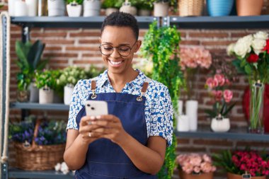 Afrikalı Amerikalı kadın çiçekçi çiçekçiye akıllı telefon kullanarak gülümsüyor.