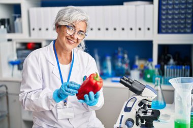 Middle age woman wearing scientist uniform analysing pepper at laboratory