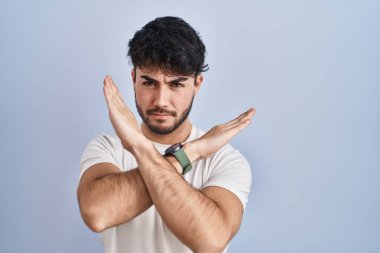 Hispanic man with beard standing over white background rejection expression crossing arms doing negative sign, angry face 