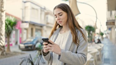 Kahve dükkanının terasında akıllı telefon kullanan genç İspanyol kadın.