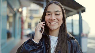 Genç, güzel İspanyol kadın, gülümsüyor. Kafe terasında akıllı telefondan konuşuyor.