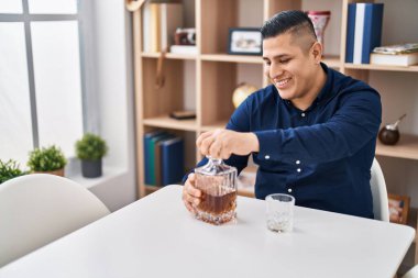 Genç Latin adam evdeki masada oturmuş viski şişesini açıyor.