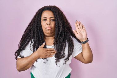 Artı, pembe arka planda duran, elleri göğsünde ve avuçları açık küfür eden, sadakat yemini eden İspanyol bir kadın. 