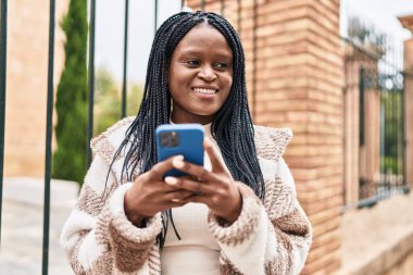 Afro-Amerikalı kadın sokakta akıllı telefon kullanarak kendine güveniyor.