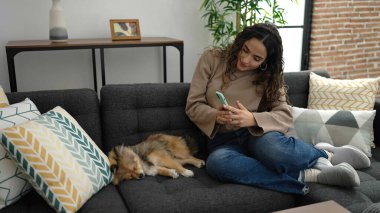Köpekli genç İspanyol kadın akıllı telefonla evde uyuyan köpeğe fotoğraf çekiyor.