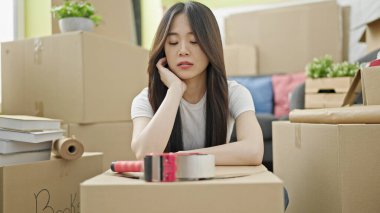 Genç Çinli kadın yeni evinde üzgün bir ifadeyle yerde oturuyor.