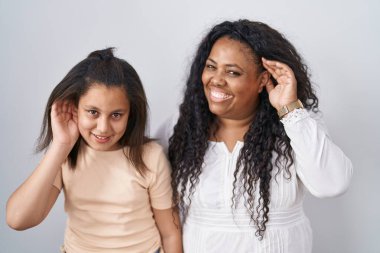 Anne ve küçük kızı, beyaz arka planda durup, el pençe divan gülümseyerek dedikoduları ve dedikoduları dinliyorlar. Sağırlık kavramı. 