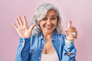 Pembe arka planda duran gri saçlı orta yaşlı kadın altı numaralı parmaklarıyla gülümseyerek kendinden emin ve mutlu bir şekilde onu işaret ediyor.. 