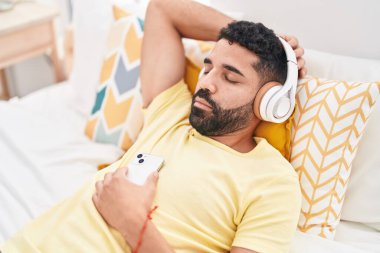 Young arab man listening to music relaxed on bed at bedroom
