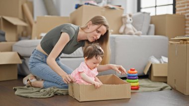 Anne ve kızı yeni evlerinde yerde oturup basketbol oyuncağıyla oynuyorlar.