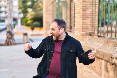 Young hispanic man smiling confident playing video game at street
