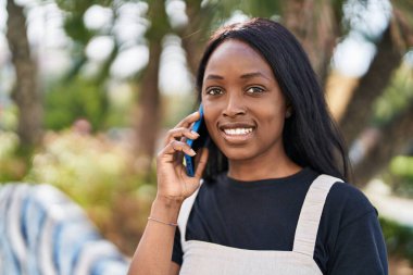 Genç Afrikalı Amerikalı kadın gülümsüyor. Parktaki akıllı telefondan konuşuyor.
