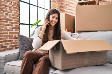 Genç, güzel, İspanyol bir kadın akıllı telefondan konuşuyor. Yeni evindeki karton kutuları açıyor.